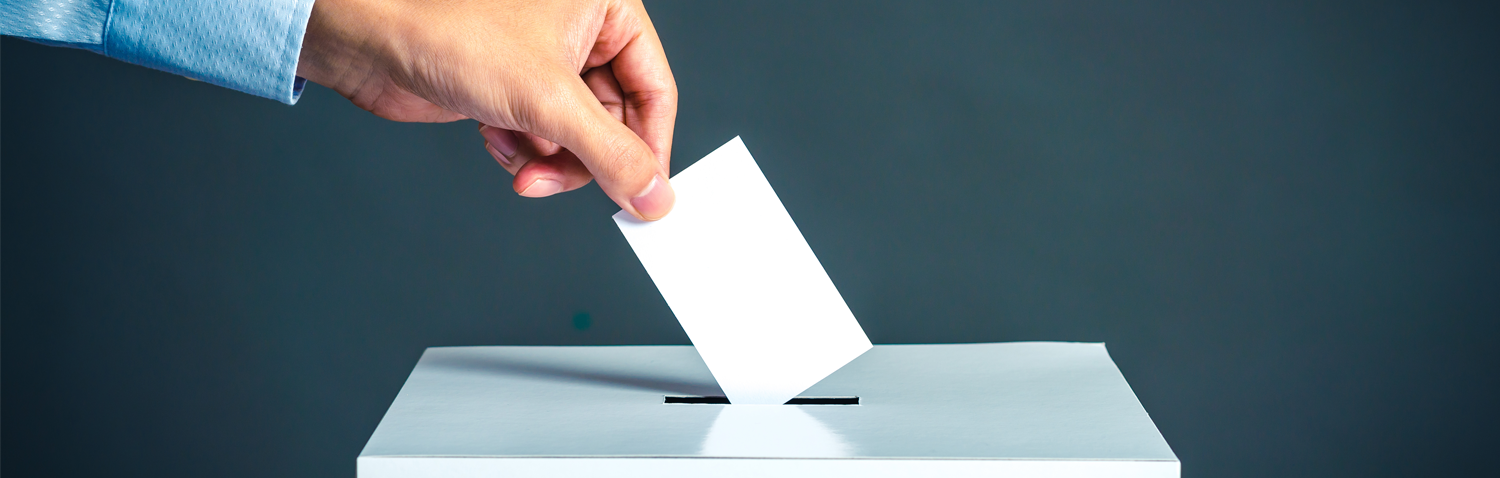 Image of a hand dropping a ballot into a box; courtesy of Shutterstock.